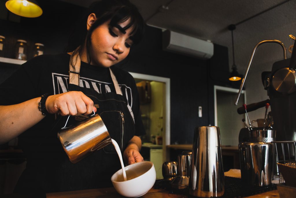 Barista pouring milk into coffee